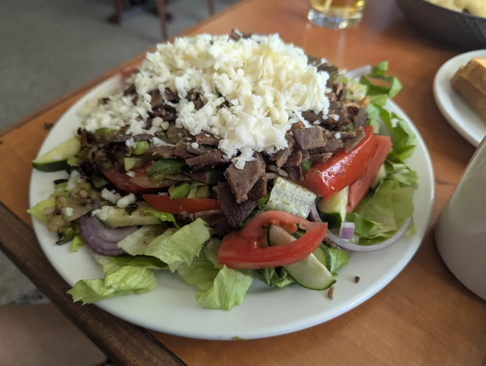 A salad topped with sliced meat, tomatoes and crumbled feta