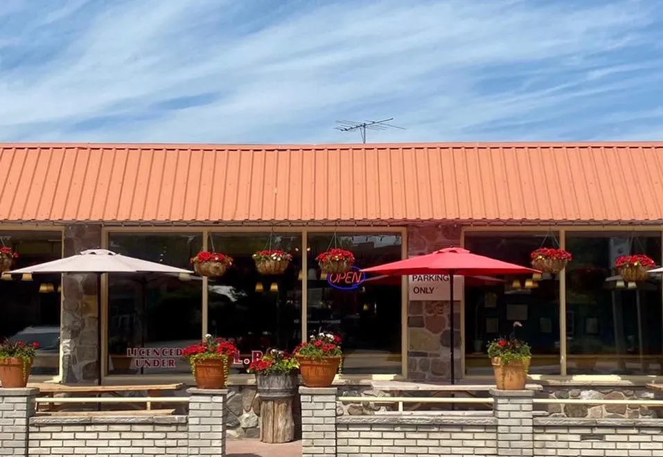Be My Guest from the street: an orange roof, red umbrellas and flower baskets over the patio